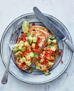 two pieces of toast with avocado and tomato on it next to a knife and fork