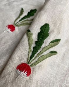 two red and white flowers are embroidered onto the linen on top of each other, along with green leaves