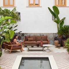 a woman sitting on a couch next to a pool surrounded by plants and potted plants