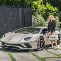 a woman standing next to a white sports car with a chanel bag on it