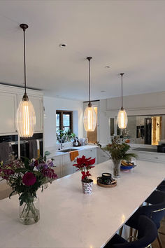 a kitchen with white counter tops and lights hanging from the ceiling over it's island