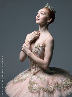 a ballerina in a pink tutu and tiara with her hands on her chest