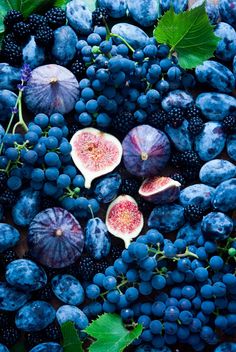 grapes, figs and other fruits are laid out on a table with green leaves