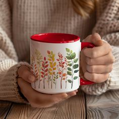 a woman holding a red and white coffee mug with colorful leaves painted on the side