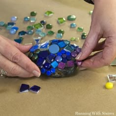 two hands are working on a rock made out of colored glass pebbles and other items