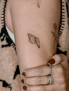 a woman's arm with a shell tattoo on her left arm and two rings around her wrist