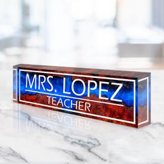 a wooden sign that reads mrs lopez teacher on it's side sitting on a marble table