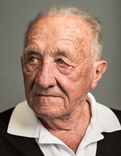 an old man with wrinkles looking at the camera while wearing a black sweater and white shirt