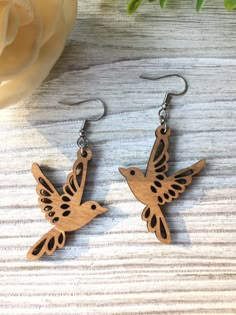 wooden earrings with laser cut hummings on the front and back of them, sitting next to a flower