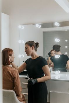 a woman getting her hair done in front of a mirror with lights on the wall