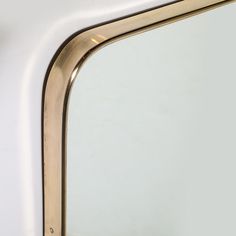 a close up of a mirror on a white wall with a gold frame and handle