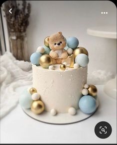 a small teddy bear sitting on top of a white cake with gold and blue decorations