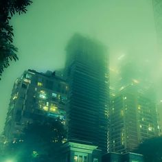 the city is very foggy at night with tall buildings in the background and street lights on