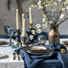 the table is set with blue linens and gold place settings, silverware, and white flowers