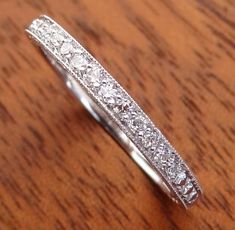 a white gold wedding band with diamonds on it sitting on top of a wooden table