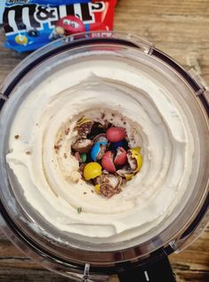 a blender filled with white frosting and candies on top of a wooden table