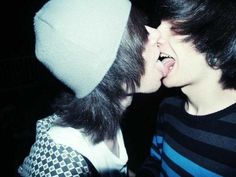 two young men are kissing each other while wearing beanies and sweaters in the dark