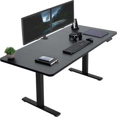 a computer desk with two monitors and a keyboard on it, next to a plant