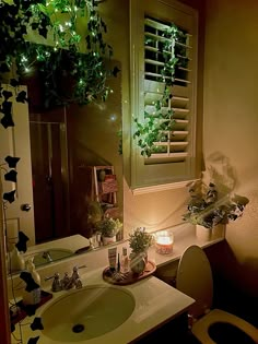 a bathroom with a sink, toilet and window covered in green plants on the wall