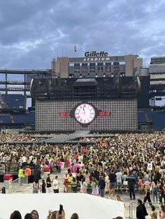 a large group of people standing in front of a stage with a clock on it