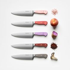 five knives are lined up next to an apple, garlic, pepper, and seasoning