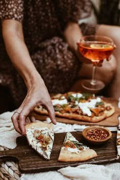 a person reaching for slices of pizza on a wooden tray next to a glass of wine