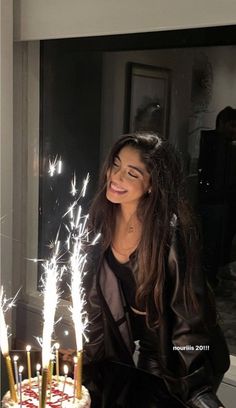 a woman sitting in front of a cake with sparklers on it and smiling at the camera