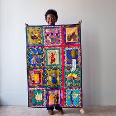 a woman holding up a colorful quilt with pictures on it