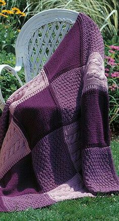 a purple and pink blanket sitting on top of a white chair next to a flower garden