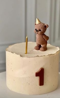 a birthday cake with a teddy bear on top and one candle in the shape of a number