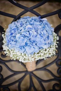 a bouquet of blue hydrangeas sitting on top of a wooden table next to a metal fence