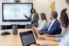 a group of people sitting around a table with laptops in front of them and a projector screen on the wall