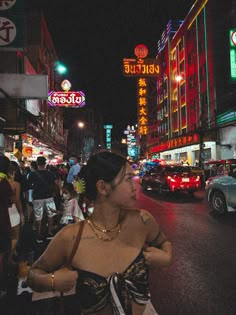 a woman standing in the middle of a busy city street at night with neon signs above her