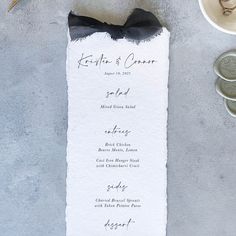 a menu card with a black bow on it next to some silver coins and a spoon