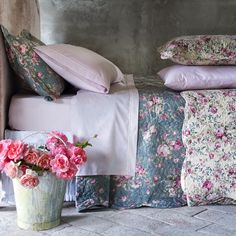 pink flowers are in a vase next to a bed with pillows and blankets on it