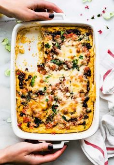 two hands holding a casserole dish with meat and vegetables in it on a white surface