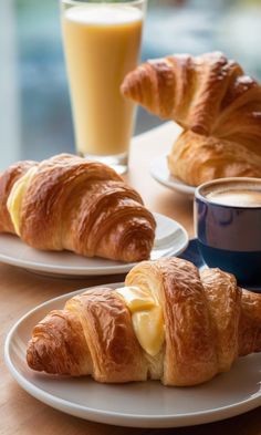 two croissants with butter on them sitting on plates next to a glass of orange juice