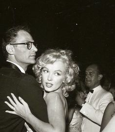 an old black and white photo of a man hugging a woman in front of other people