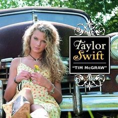 a woman sitting on the ground next to an old car with taylor swift's logo