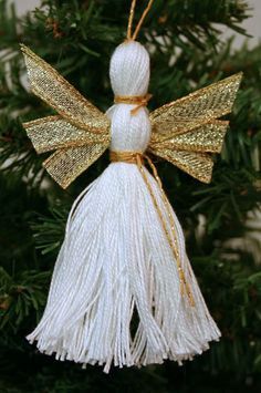 a white ornament hanging from a christmas tree with gold trim and tassels