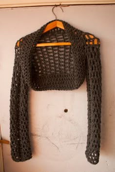 a crocheted sweater hanging on a wall next to a coat hanger with an orange ribbon