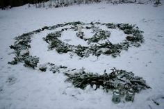 a circle made out of plants and jars in the middle of snow covered ground with trees behind it