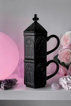 a black coffee mug sitting on top of a table next to pink flowers