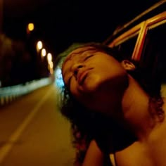 a woman laying on the side of a road at night with her eyes closed and head down