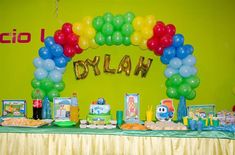 a birthday party with balloons and decorations on the table in front of a green wall