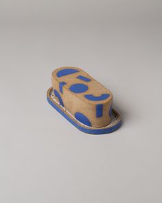 a small blue and brown hat sitting on top of a white table next to a gray wall