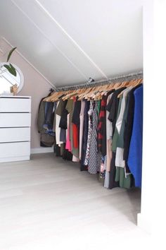 an attic closet with clothes hanging from the ceiling and drawers on the floor, next to a white chest of drawers