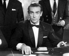 a man in a tuxedo sitting at a table with three other men behind him