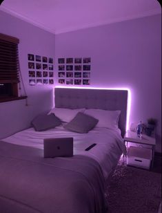 a laptop computer sitting on top of a bed in a room with purple lighting around it