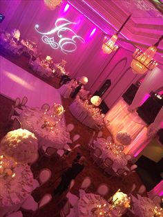 a banquet hall with tables and chairs covered in white linens, lit by chandeliers